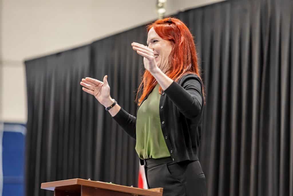 Rach signing at a podium during a talk