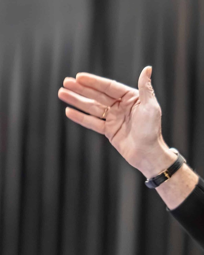 Close-up of an open hand mid-sign against a dark stage curtain